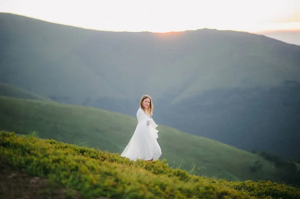 O femeie îmbrăcată într-o rochie de mireasă traversează câmpul spre munți — Fotografie, imagine de stoc