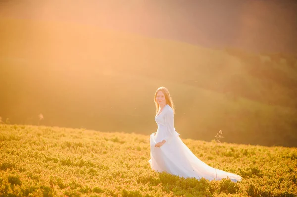 O femeie îmbrăcată într-o rochie de mireasă traversează câmpul spre munți — Fotografie, imagine de stoc