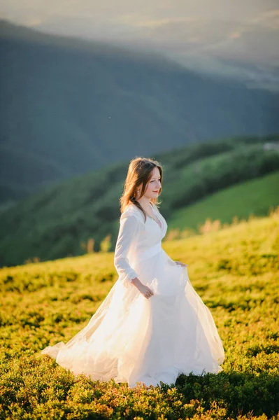 Vrouw in een trouwjurk loopt over het veld richting de bergen — Stockfoto