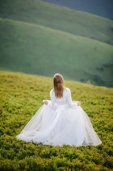 Женщина в свадебном платье бежит через поле к горам — стоковое фото