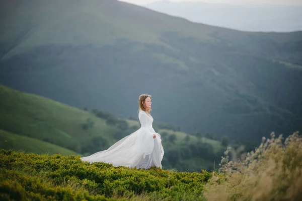 Donna in abito da sposa corre attraverso il campo verso le montagne — Foto Stock