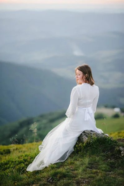 O femeie îmbrăcată într-o rochie de mireasă traversează câmpul spre munți — Fotografie, imagine de stoc