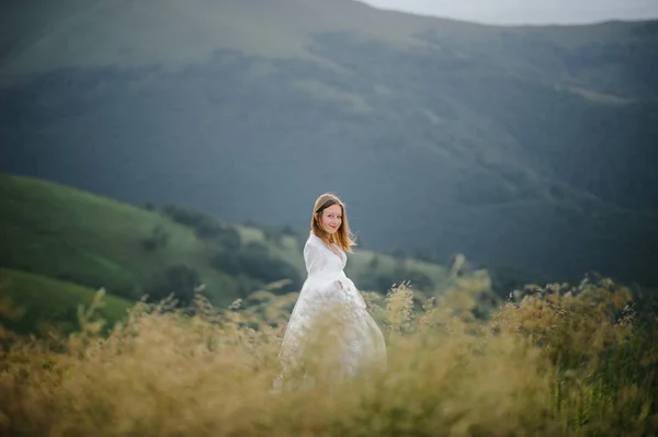 O femeie îmbrăcată într-o rochie de mireasă traversează câmpul spre munți — Fotografie, imagine de stoc