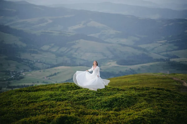 O femeie îmbrăcată într-o rochie de mireasă traversează câmpul spre munți — Fotografie, imagine de stoc