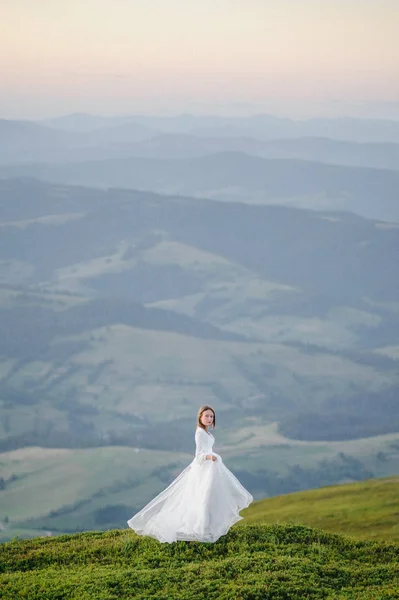 Kobieta w sukni ślubnej działa przez pole w kierunku gór — Zdjęcie stockowe