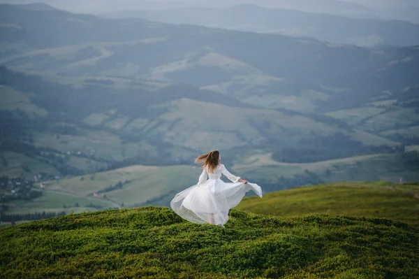 Женщина в свадебном платье бежит через поле к горам — стоковое фото