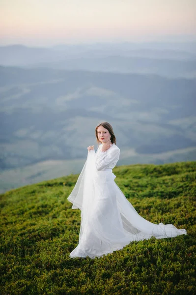 Kobieta w sukni ślubnej działa przez pole w kierunku gór — Zdjęcie stockowe