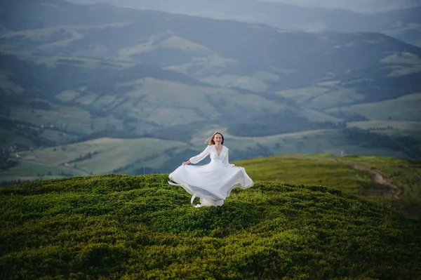 O femeie îmbrăcată într-o rochie de mireasă traversează câmpul spre munți — Fotografie, imagine de stoc