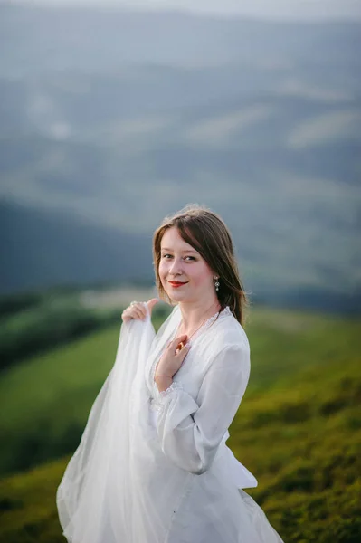 Vrouw in een trouwjurk loopt over het veld richting de bergen — Stockfoto