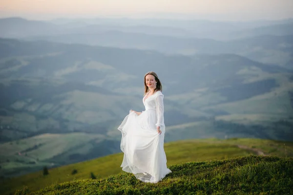 O femeie îmbrăcată într-o rochie de mireasă traversează câmpul spre munți — Fotografie, imagine de stoc