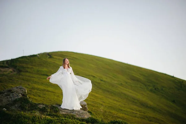 Donna in abito da sposa corre attraverso il campo verso le montagne — Foto Stock