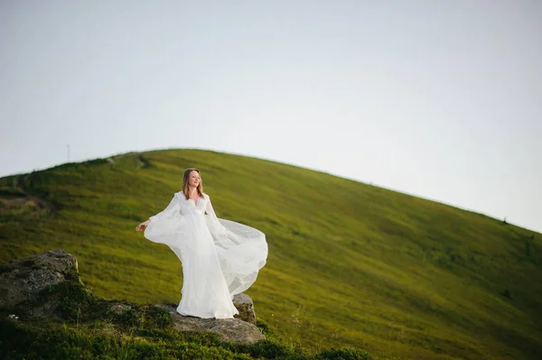 O femeie îmbrăcată într-o rochie de mireasă traversează câmpul spre munți — Fotografie, imagine de stoc