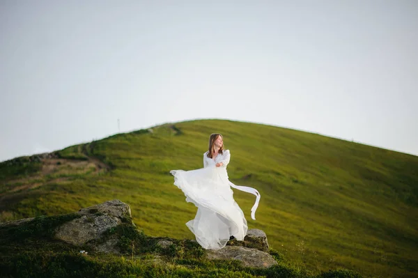 O femeie îmbrăcată într-o rochie de mireasă traversează câmpul spre munți — Fotografie, imagine de stoc