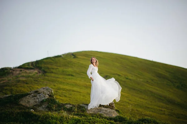 O femeie îmbrăcată într-o rochie de mireasă traversează câmpul spre munți — Fotografie, imagine de stoc