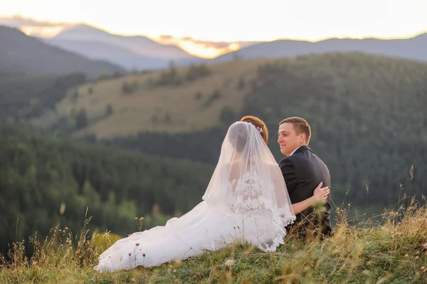 在山上拍婚纱照新婚夫妇背靠在草地上坐着互相望着 — 图库照片