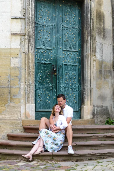 Two lovers are sitting on the steps of an old church. The guy hugs the girl from behind. The couple is happy.
