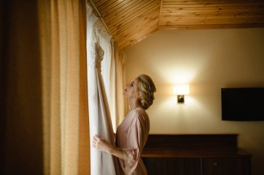 Genç, sarışın gelin gelinliğine bakıyor..