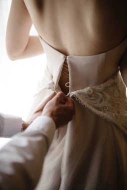 Beyaz, lüks elbiseli, güzel, sarışın gelin düğüne hazırlanıyor. Sabah hazırlıkları. Bir kadın elbise giyer. Damat geline yardım eder..