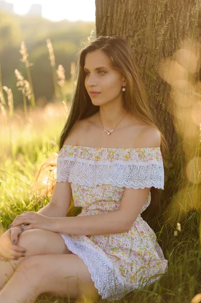 一个穿着太阳衣的年轻漂亮姑娘的画像 日落时在公园举行的夏季摄影会 一个女孩坐在树荫下 — 图库照片