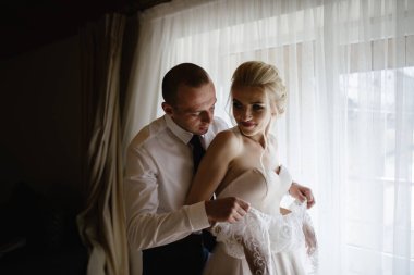 Beyaz, lüks elbiseli, güzel, sarışın gelin düğüne hazırlanıyor. Sabah hazırlıkları. Bir kadın elbise giyer. Damat geline yardım eder..