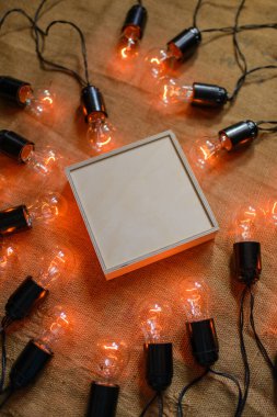 Çuval bezi arka planında bir kutu kontrplak. Kutunun etrafında Edison lambaları olan eski bir çelenk var. Boş alan.