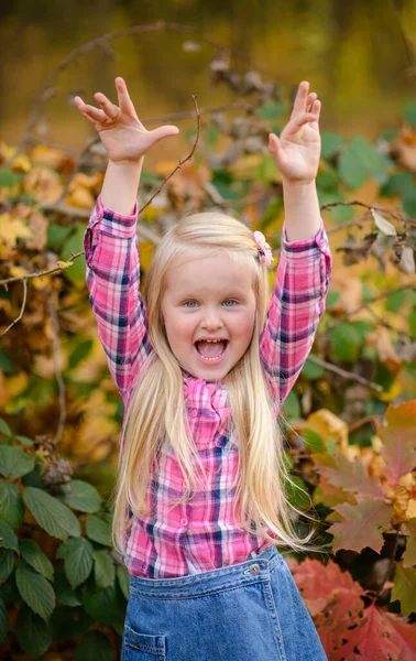 穿着衬衫和牛仔短裤的金发小女孩在秋天的公园里散步 — 图库照片
