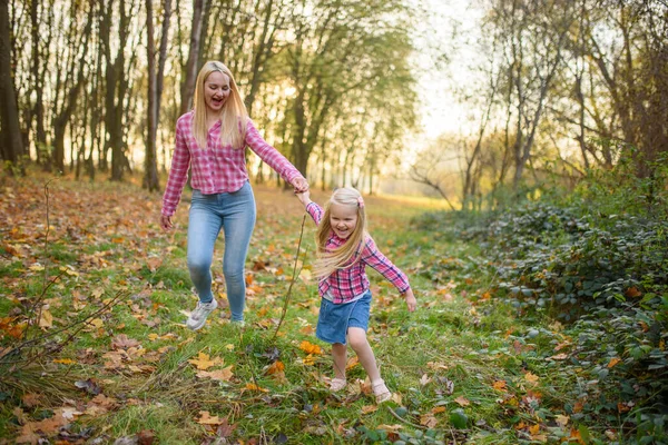 Mom and daughter in jeans and pink shirts walk in the autumn park.