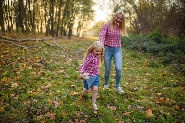 Mom and daughter in jeans and pink shirts walk in the autumn park.