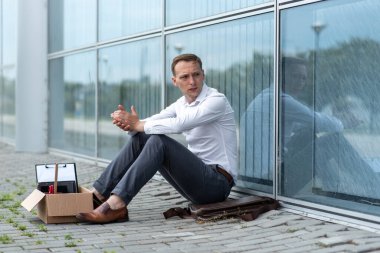 Kovulmuş bir ofis çalışanı modern bir ofis binasının yanında yerde oturuyor. Adam işten çıkarılma konusunda çok endişeli. Adam yüzünü çevirir ve el sıkışır..