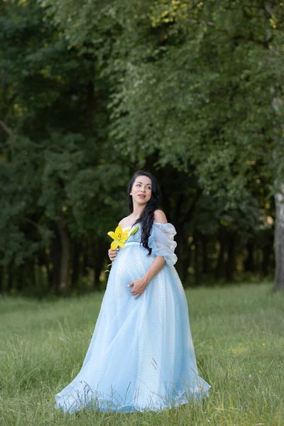 緑の木の背景に青いドレスを着た妊婦 — ストック写真