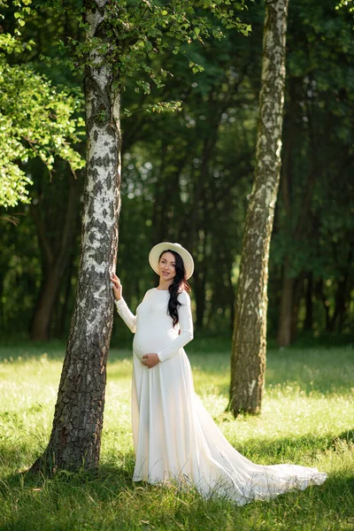 Ciężarna Kobieta Kapeluszu Pozująca Białej Sukience Tle Zielonych Drzew — Zdjęcie stockowe
