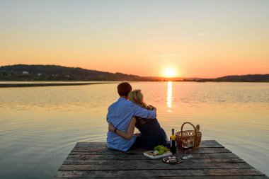 Kadın ve erkek gölün yanındaki iskelede piknik yapıyorlar..