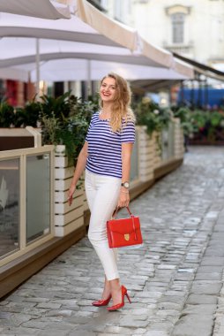 Genç ve güzel bir kadın eski şehrin sokaklarında poz veriyor. Kadının kırmızı bir çantası var..