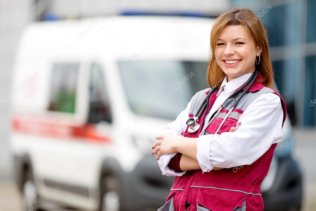 Medical concept. Happy paramedic female with phonendoscope at emergency car background