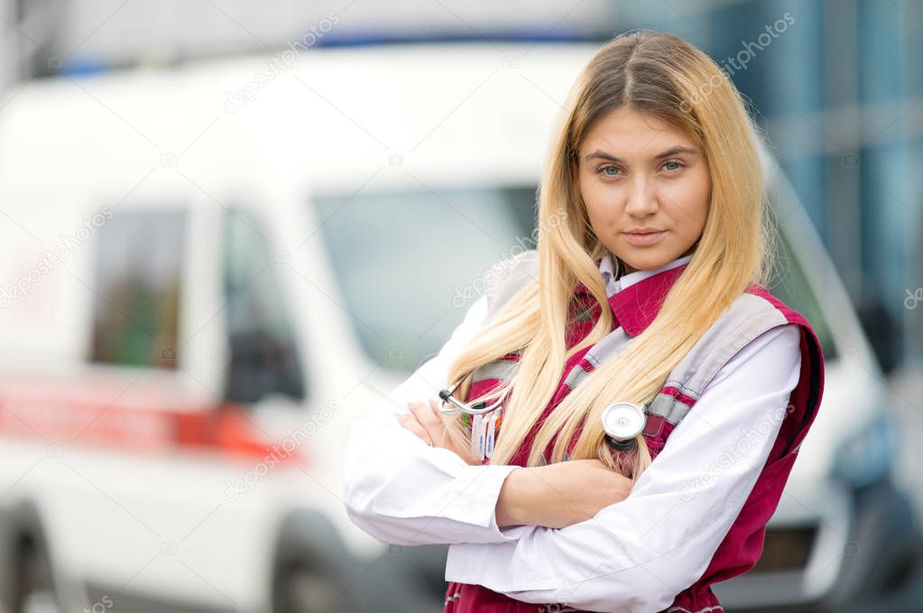 Medical concept.Young paramedic female with phonendoscope at emergency car background