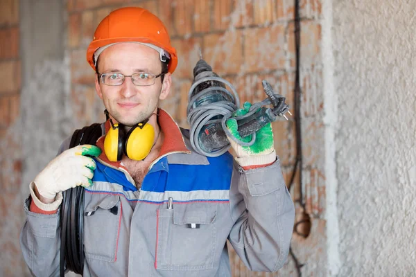 电工人建筑工人与电缆和冲床钻具在房子墙壁背景 — 图库照片