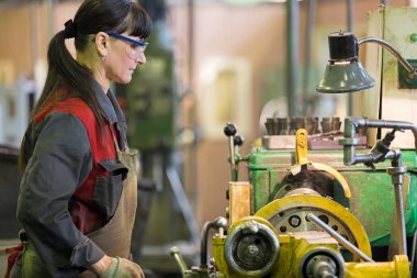 Metalwork industry. Factory woman turner working at workshop lathe machine clipart