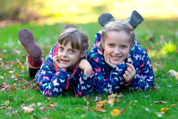 秋の葉を持つ緑の草の上に横たわる2人の笑顔の兄弟の女の子 — ストック写真