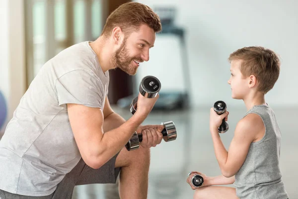 Little kid training with dumbbells together with father at fitness center — Stock Photo
