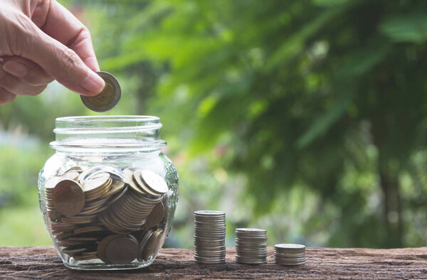 Hand drop a coin in glass jar with money coin stack growing for business. financial and accounting concept.