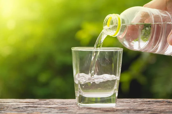 Weibliche Hand Gießt Wasser Von Flasche Glas Auf Naturhintergrund — Stockfoto