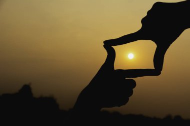 Gün batımı ile çerçeve hale eller. Çerçeve jest yapma kadın elinde yakın çekim.