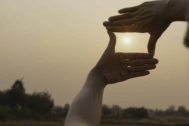 Gün batımı ile çerçeve hale eller. Çerçeve jest yapma kadın elinde yakın çekim.