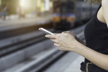 Tren bekleyen ve akıllı telefon kullanan bir kadın.