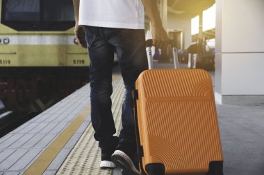 Turuncu bavul taşıyan bir adam, tren yolunda yürüyor.