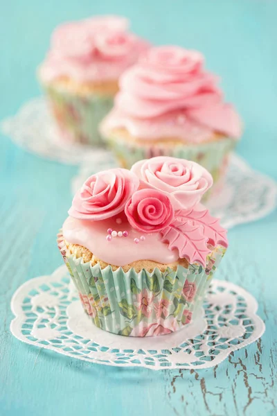 青い木製の背景にピンクの花のカップケーキ — ストック写真