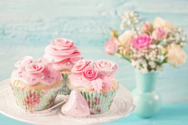 Mavi ahşap arka plan üzerinde pembe çiçekler ile cupcakes