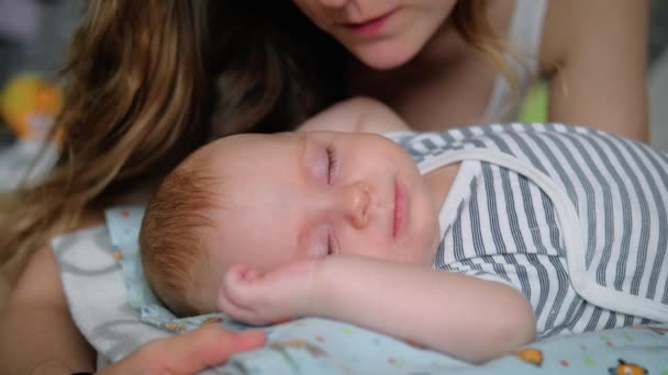Junge Mutter küsst ihr kleines schlafendes Neugeborenes — Stockvideo