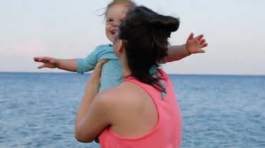 Küçük bebek kız ile genç anne yaz gününde bir plajda eğlenin. Mutlu aile konsepti. Mutlu çocukluk. 4k video görüntüleri