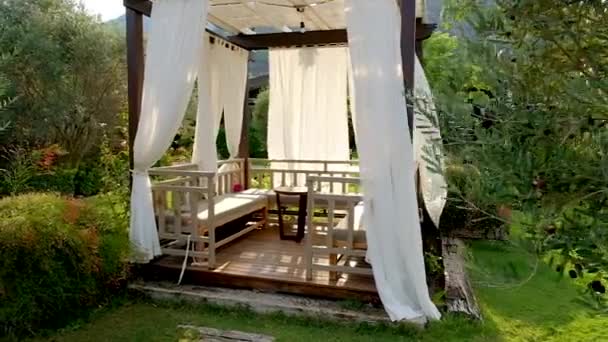 Gazebo extérieur en bois avec rideaux blancs. Pavillon de jardin au coucher du soleil dans la journée d'été.1920x1080 Full HD Slow motion video footage. Plan de suivi .